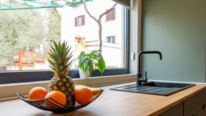 A kitchen counter with a fruit bowl containing a pineapple and oranges, a modern faucet, and a view of a building through a window.