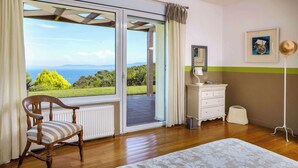 A bedroom with a large sliding glass door leading to a balcony, a wooden chair, a white dresser, and a floor lamp.