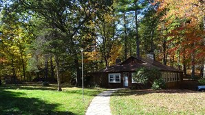 A small cabin with a paved path leading to it, surrounded by trees with autumn foliage.