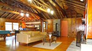 A spacious living area with a wooden ceiling, a sofa, a coffee table, a fireplace, and a bar area with bottles.