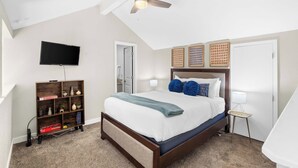 Um quarto com cama, ventilador de teto, televisão, estante de livros e mesa de cabeceira.