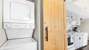 Uma cozinha com máquina de lavar branca, porta de madeira e armários brancos.