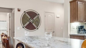 Een keuken met een marmeren aanrecht, twee wijnglazen, houten stoelen en een decoratieve wandversiering.