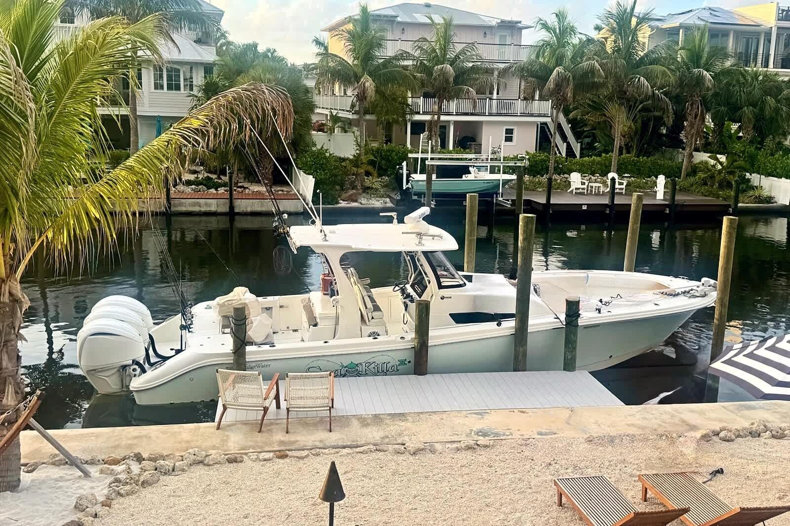 A boat docked at a marina with a sandy beach area and palm trees in the background.