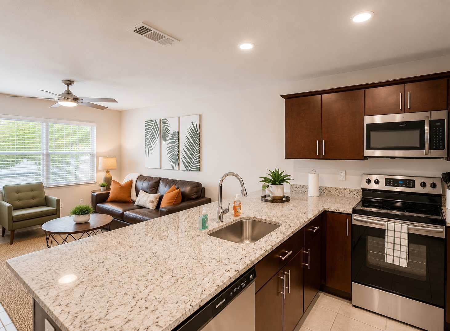 A modern kitchen with granite countertops, stainless steel appliances, and a dining area with a leather couch and a small table.