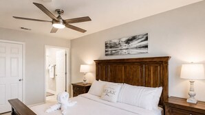 A neatly made bed with a wooden headboard, a ceiling fan, a wall-mounted painting, and bedside lamps. - Family & Pet Friendly-Sleeps 4 (Apollo Beach)