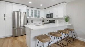 A modern kitchen with white cabinetry, stainless steel appliances, a central island with stools, and a backsplash with a geometric pattern.