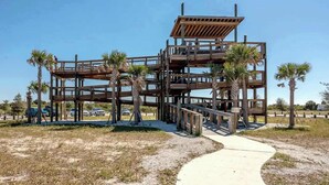 A multi-level wooden structure with a walkway leading to it, surrounded by palm trees.