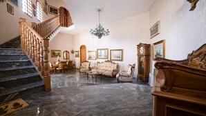 A grand staircase leading to an upper floor, a chandelier, and a seating area with ornate furniture. - Il rifugio del templare  - Appartamento Paggio (Roccavaldina)
