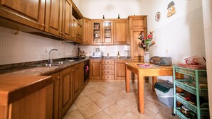 A kitchen with wooden cabinets, a sink, a stove, a microwave, and a dining table. - Il rifugio del templare  - Appartamento Paggio (Roccavaldina)