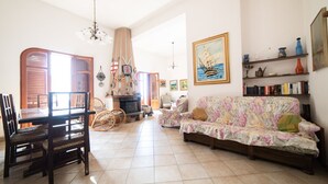 A spacious living room with a fireplace, a sofa, a dining table with chairs, and a bookshelf. - Il rifugio del templare  - Appartamento Paggio (Roccavaldina)