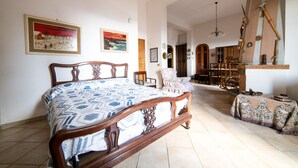 A spacious bedroom with a large bed, a wooden chair, and a dining area with chairs and a table. - Il rifugio del templare  - Appartamento Paggio (Roccavaldina)