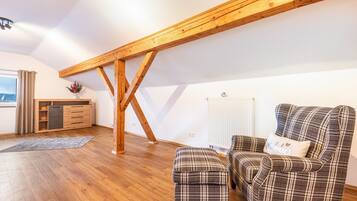 Een loft-achtige kamer met houten balken, een bank, een voetenbankje en een kleine tafel met een bloevas.