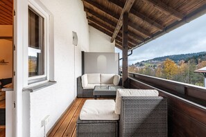 Un balcon agrémenté de meubles en osier, un mur blanc et une vue sur un paysage vallonné.