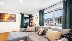 En moderne stue med en grå sofa, et træbord, et billede og et stort vindue med gardiner.
