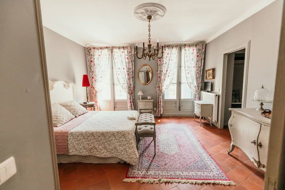 A bedroom with a bed, a chair, a dresser, a mirror, and a chandelier.