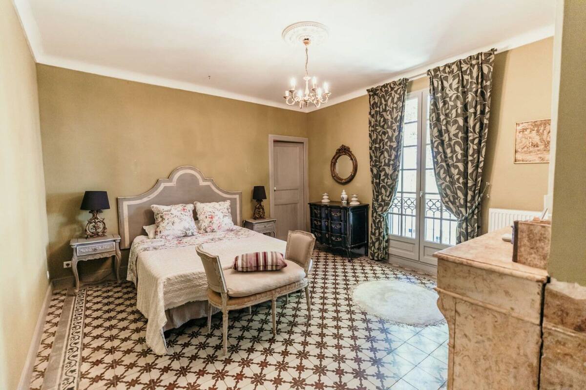 A bedroom with a bed, a chair, a dresser, a mirror, and a window with curtains.