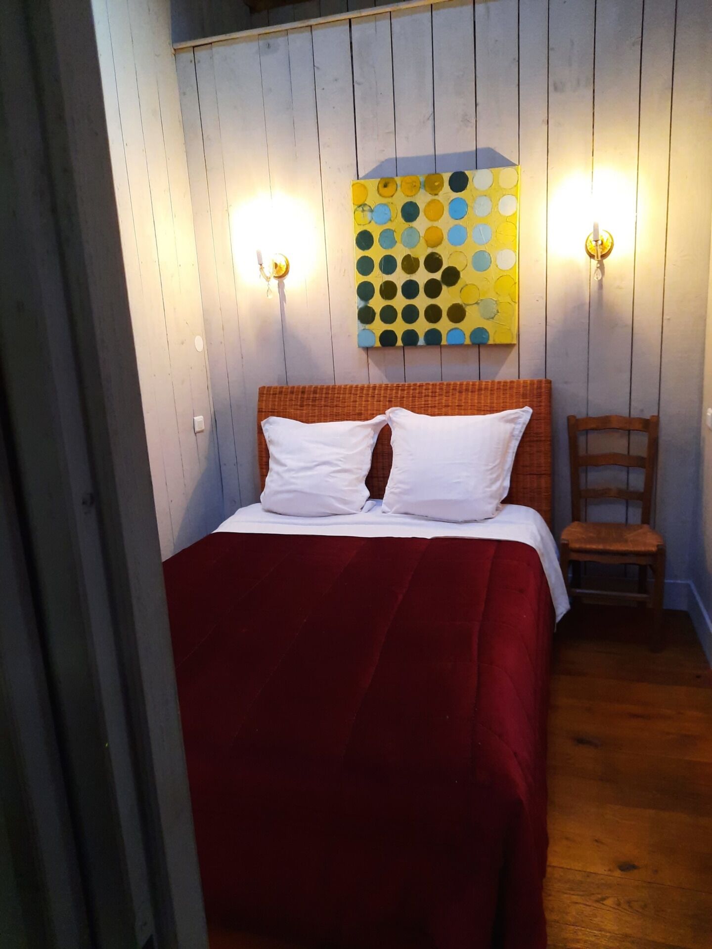A room with a bed, a chair, and a wall-mounted artwork.
