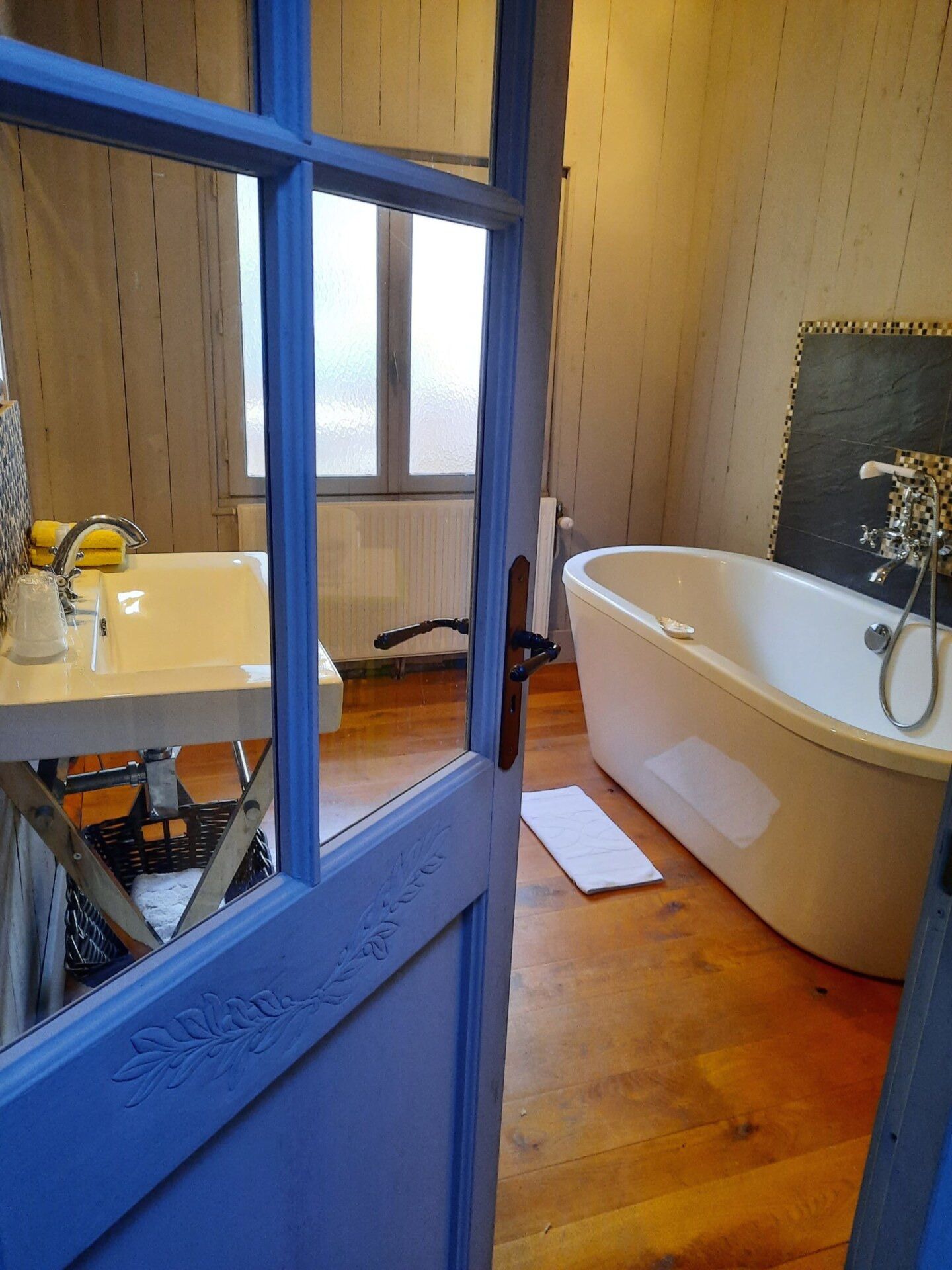 Een badkamer met een houten vloer, een witte badkuip, een wastafel en een raam.