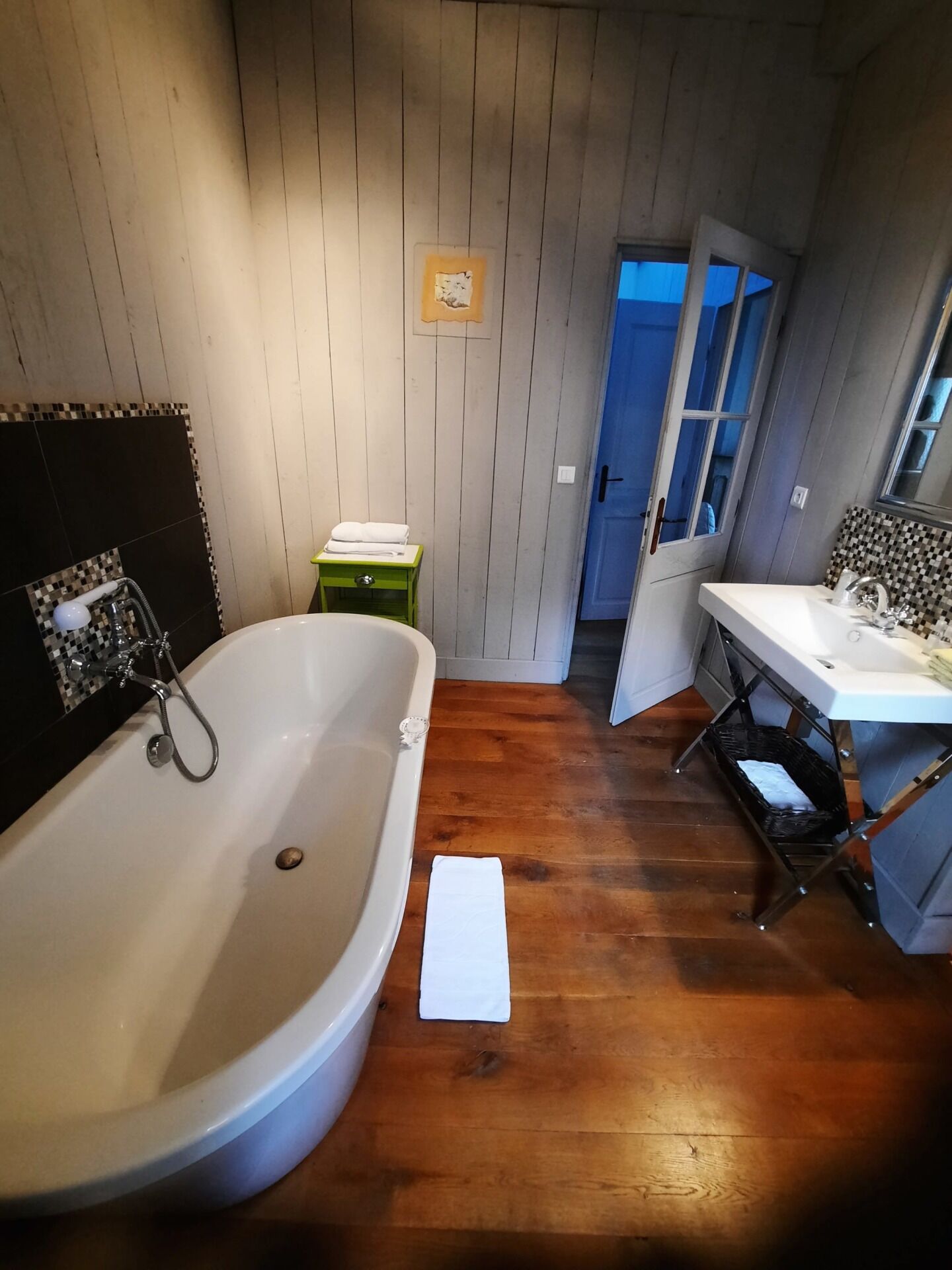 A bathroom with a freestanding bathtub, a sink with a mirror, and wooden flooring.