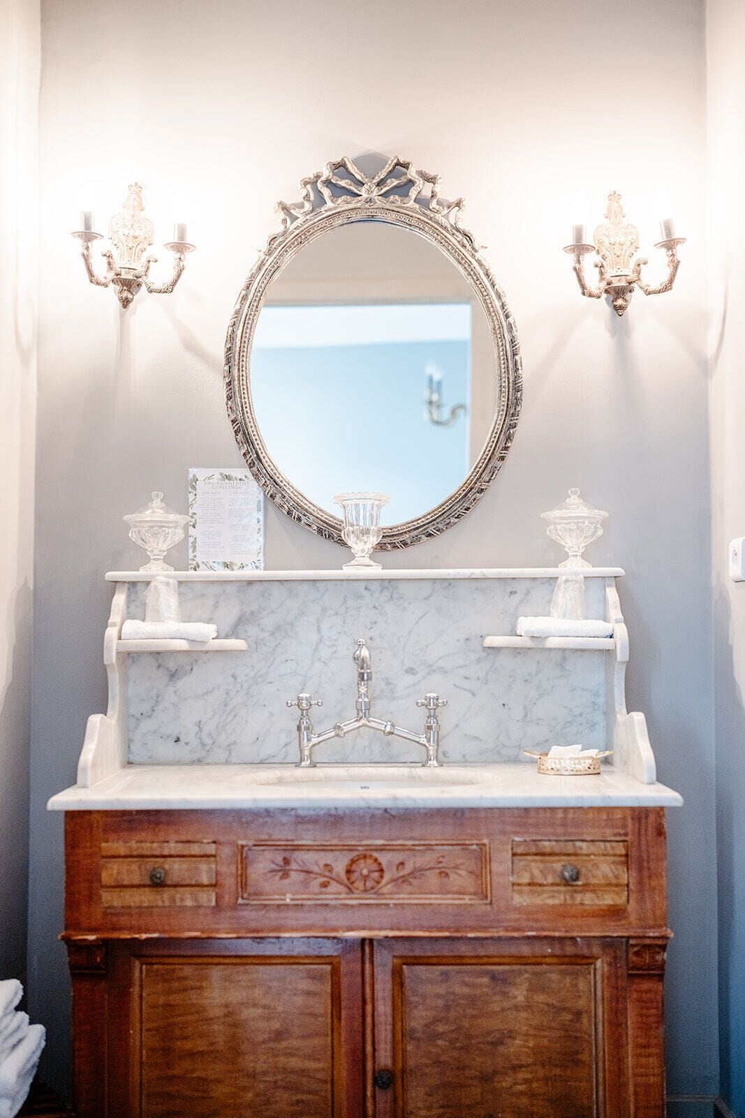 Une salle de bain avec un lavabo en marbre, un miroir doté d’un cadre orné et des appliques murales.