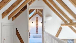 Un couloir étroit mène à une chambre dont le plafond est en pente et où les poutres en bois sont apparentes.