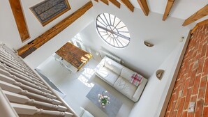 Un intérieur moderne avec un escalier, une lucarne circulaire, un canapé blanc et un coin repas.