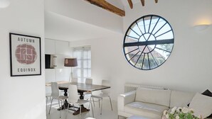 Un salon moderne avec un coin repas, des meubles blancs, une grande fenêtre circulaire et un tableau encadré au mur.
