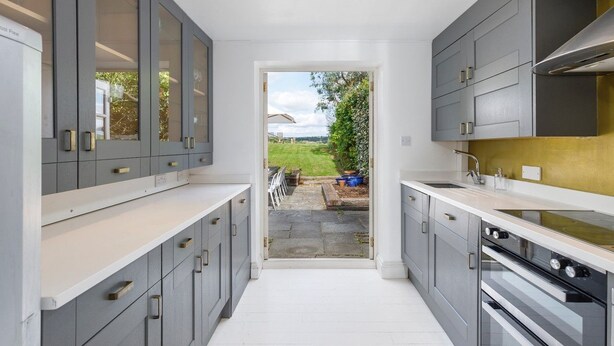 Une cuisine moderne avec des meubles gris, des plans de travail blancs et une vue sur l’extérieur.