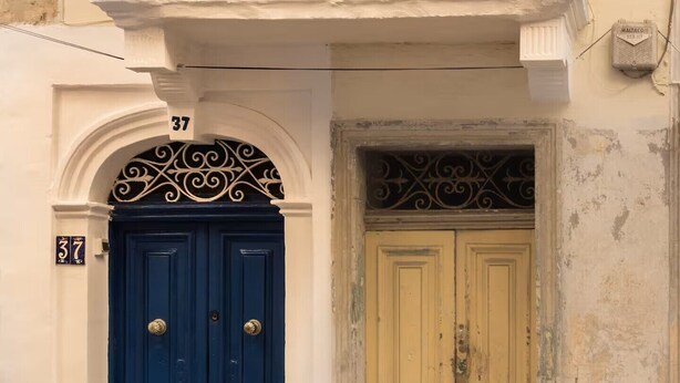Ein Gebäude mit blauer Tür und einem gelben Obergeschoss mit Balkon.