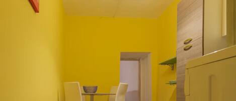 Une cuisine de taille réduite avec des murs jaunes, un plancher en bois, une table à manger avec des chaises et un luminaire suspendu.