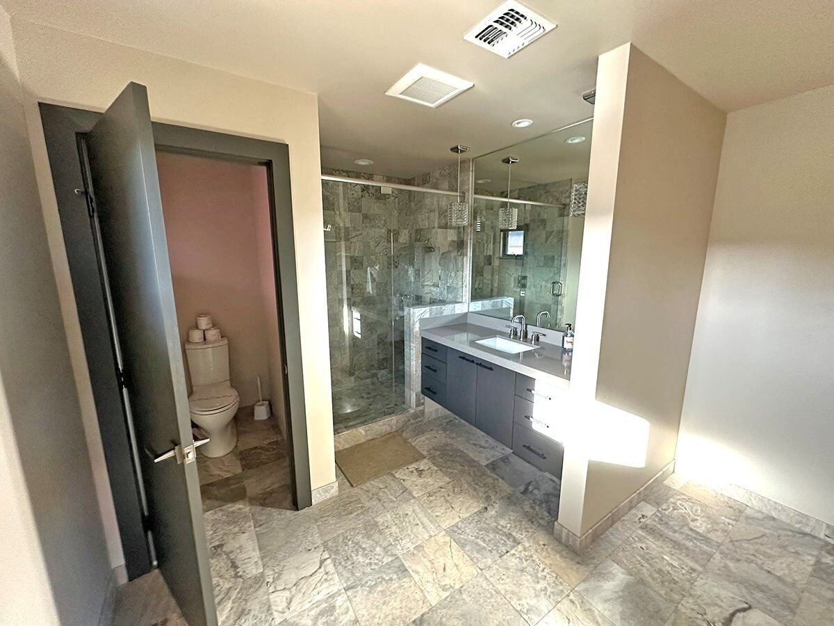 A modern bathroom with a glass shower enclosure, a large mirror, and a marble-tiled floor.