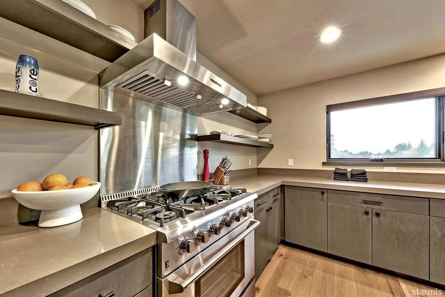 A modern kitchen with stainless steel appliances, a bowl of oranges, and a window with a view.