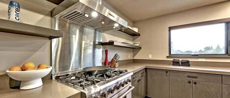 A modern kitchen with stainless steel appliances, a bowl of oranges, and a window with a view.