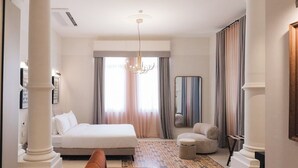 Hotellihuone, jossa on sänky, sohva, peili ja kattokruunu.
