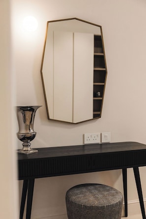 A mirror with a geometric frame, a black console table, and a patterned ottoman.