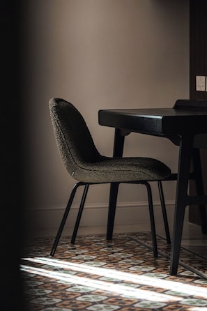 A chair with a textured seat and backrest, a table with a dark surface, and a patterned floor.
