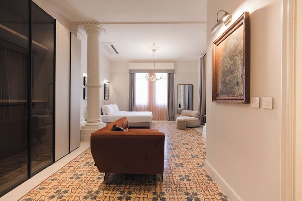 A hotel room with a large bed, a sofa, a chandelier, and a patterned carpet.