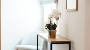 A white chair, a wooden table with a potted orchid, and a framed picture on the wall. - Elegant two-bedroom designer apartment near Balluta Bay, combining Maltese heritage charm with modern comfort. (St. Julian's)