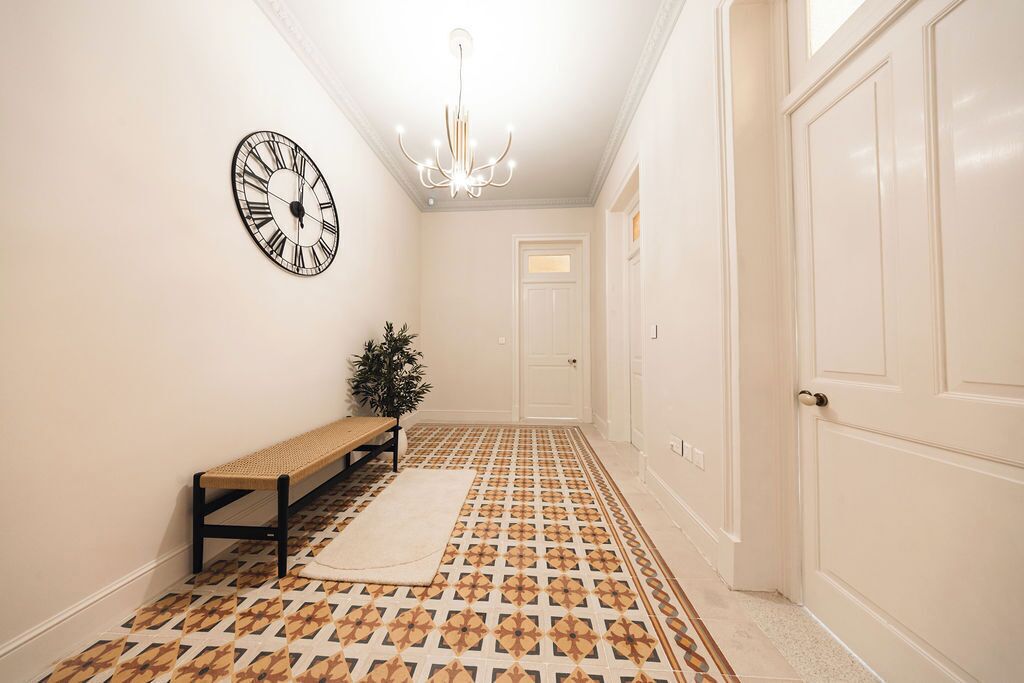 A hallway with patterned flooring, a bench, a wall clock, and a door.