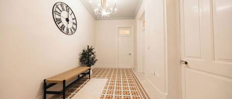 A hallway with patterned flooring, a bench, a wall clock, and a door.