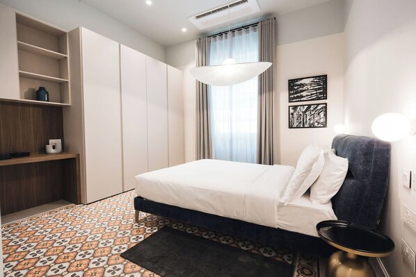 A bedroom with a bed, a wardrobe, a shelf with a vase, a patterned rug, and a window with curtains.