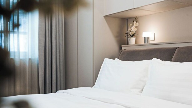 A hotel room with a bed, curtains, a nightstand with a lamp, and a potted plant. - Elegant two-bedroom designer apartment near Balluta Bay, combining Maltese heritage charm with modern comfort. (St. Julian's)
