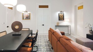 A modern interior with a dining table, chairs, a sofa, and a small side table with a lamp. - Elegant two-bedroom designer apartment near Balluta Bay, combining Maltese heritage charm with modern comfort. (St. Julian's)