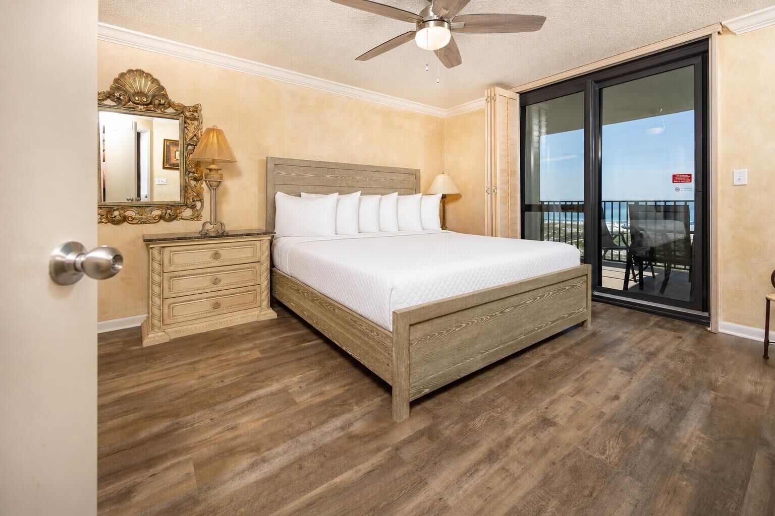 A bedroom with a bed, a nightstand, a dresser, a ceiling fan, and a sliding glass door to a balcony.