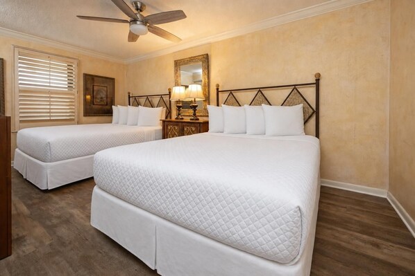 Une chambre d’hôtel avec deux lits «
queen size
», un ventilateur de plafond, une table de chevet avec une lampe et un grand miroir au mur.