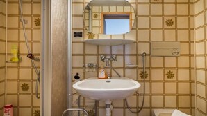 A bathroom with a white sink, a mirror above it, and a shower area with a showerhead and control panel. - Hotel Sterne - Standard Apartment with Lake view (Beatenberg)