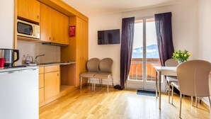 A compact kitchen with wooden cabinets, a microwave, and a dining area with chairs and a table. - Hotel Sterne - Standard Apartment with Lake view (Beatenberg)