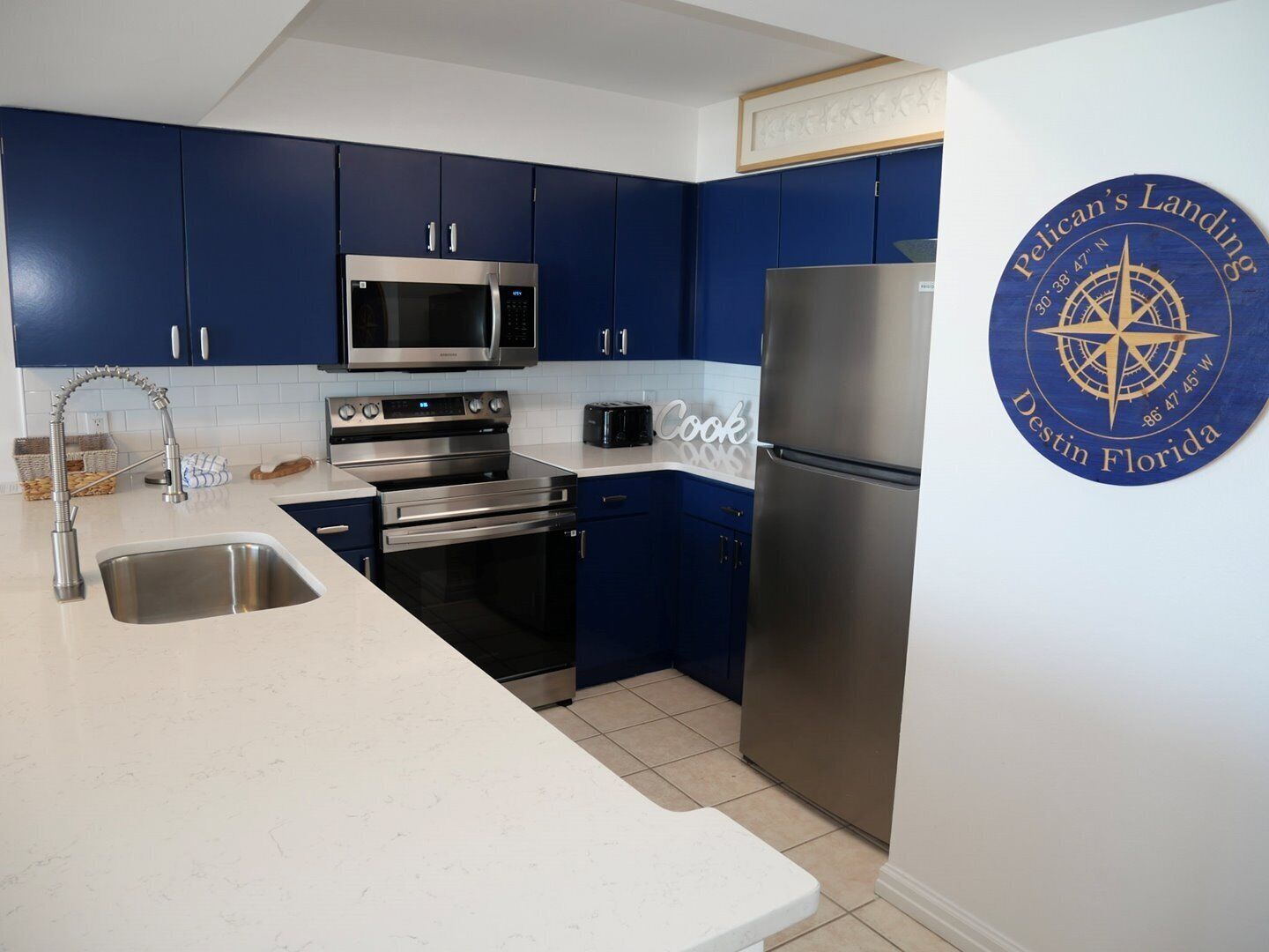 Een moderne keuken met blauwe kastjes, roestvrijstalen apparatuur en een wit aanrecht.