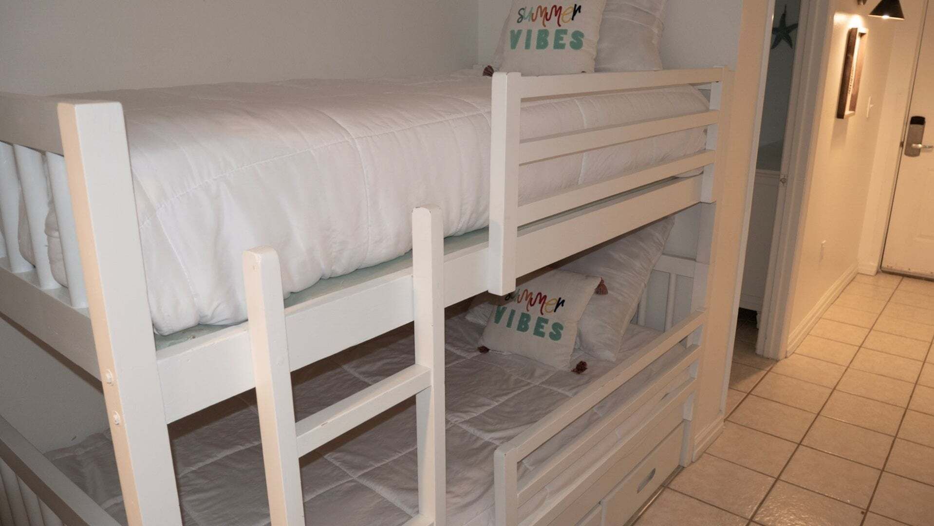 A bunk bed with pillows labeled 'Summer Vibes' in a room with a tiled floor.